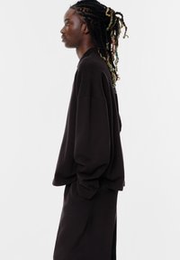 Overmaat zwart sweatshirt van zacht materiaal, met verlaagde schouders en geribde zoom. Gecombineerd met bijpassende zwarte broek voor een samenhangende look.