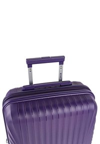 Maleta dura de color púrpura con textura de surcos verticales, un asa telescópica plateada y cierre de cremallera. Diseño compacto y ligero.