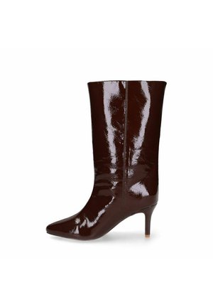 Donkerbruine glanzende leren laars tot halfvering met puntige neus en slanke, middelhoog hak, getoond vanaf de buitenkant tegen een witte achtergrond.