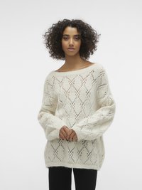Pull en tricot crème avec un motif en losange ouvert, un large col et de longues manches volumineuses. Texture douce, coupe décontractée.