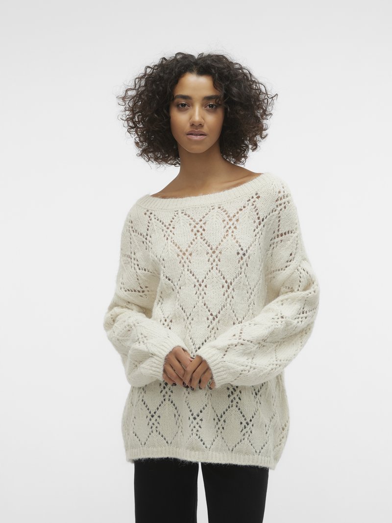Pull en tricot crème avec un motif en losange ouvert, un large col et de longues manches volumineuses. Texture douce, coupe décontractée.