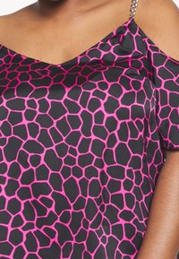 Haut noir présentant un motif nid d'abeille rose, avec un col en V et une conception à épaules découvertes. Tissu texturé avec des accents de chaîne métallique sur les bretelles.