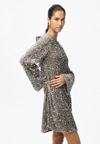 Λαμπερό καφέ φόρεμα διακοσμημένο με ασημί παγιέτες, με μακριά μανίκια σε σχήμα καμπάνας, στρογγυλή λαιμόκοψη και χαλαρή γραμμή, με ελαφρώς υφή στην επιφάνεια.