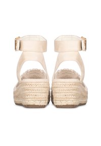 Sandalias de esparto beige con una correa de tobillo de ante y una suela de yute trenzado. Plataforma gruesa, parte trasera abierta y detalles de punta redondeada. Accento en hardware dorado.