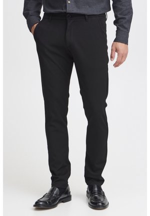 Czarne dopasowane spodnie wykonane z gładkiego materiału, z tradycyjnym zapięciem na guzik, bocznymi kieszeniami i dopasowanym krojem.