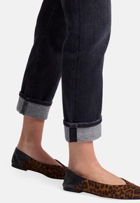 Jeans en denim foncé avec des poignets roulés, associés à des ballerines en imprimé léopard avec un talon noir et des côtés ouverts. Tissu texturé et couleurs contrastées.