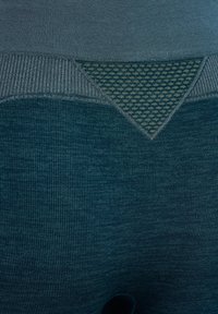 Zbliżenie na turkusową dzianinę o prążkowanej fakturze z wzorzystą trójkątną naszywką w kontrastujących odcieniach niebieskiego i szarości.