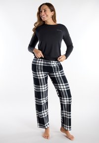 Top negro de manga larga con cuello redondo; pantalones de franela gris y blanco a cuadros con perneras anchas y cintura elástica.