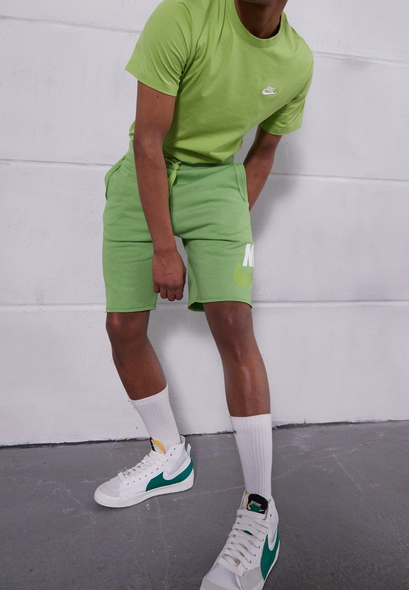Personne portant un T-shirt et un short Nike vert citron, avec des chaussettes blanches et des baskets blanches avec le logo Nike vert.