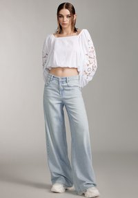 Top corto blanco con mangas de encaje y vaqueros ligeros de tiro bajo, acompañado de zapatillas blancas. Tejido suave y corte relajado.