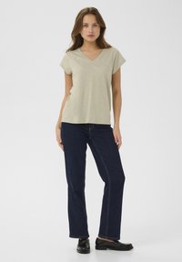 Ljusgrön V-ringad t-shirt med korta ärmar, kombinerad med mörkblå raka jeans och svarta skor. Slät tyg, avslappnad passform.