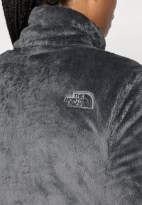 Halli fleece-jakk, millel on kõrge krae. Omab pehmet tekstuuri ja tikitud brändi logo kaeluse lähedal seljaosas.
