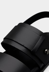 Μαύρο δερμάτινο σανδάλι με δύο φαρδιές λουράκια, λεία υφή και διακοσμητικό καρφί ασημί αποχρώσεις. Καμπυλωτός σχεδιασμός με ανοιχτή φτέρνα.