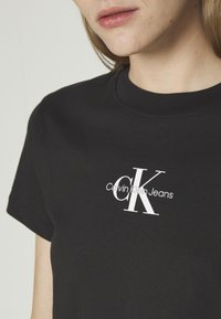 Zwarte katoenen T-shirt met korte mouwen, voorzien van een wit Calvin Klein Jeans-logo dat in een moderne lettertype op de voorkant is gedrukt.