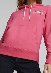 Sudadera de mikrofibra rosa con un bolsillo frontal, que cuenta con cordones, puños acanalados y un pequeño logo bordado. Textura suave y corte relajado.