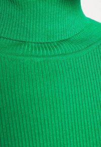 Gros plan d’un pull à col roulé en tissu côtelé vert vif montrant le motif tricoté texturé et les plis du col.