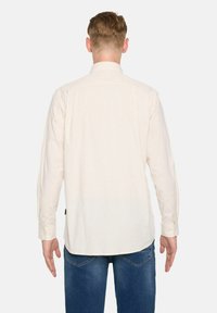 Langarmhemd in Creme mit dezenten vertikalen Streifen, mit einem Button-Down-Kragen und schlichtem Rücken, kombiniert mit blauen Jeans.