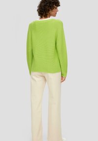 Jasnozielony sweter z dzianiny z szerokim dekoltem i prążkowaną fakturą, w połączeniu z kremowymi spodniami o szerokich nogawkach. Prosty i nowoczesny design.