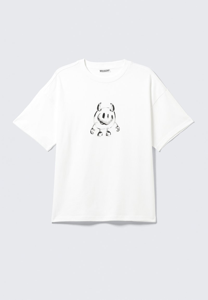 T-shirt blanc en coton à manches courtes avec un dessin de personnage de dessin animé noir avec des cornes et les bras positionnés au centre.