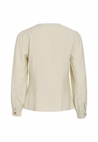 Blusa beige chiaro a maniche lunghe con un fit rilassato, scollatura rotonda e polsini con bottone. Tessuto liscio, leggermente testurizzato con cuciture laterali.