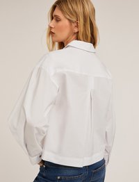 Witte crop top gemaakt van katoen met een achterste plooi, brede mouwen, een puntige kraag en metalen knopen bij de manchetten.