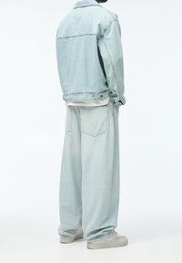 Světlě modrá džínová bunda a odpovídající volné kalhoty s přehnanou siluetou a minimálními kovovými doplňky, texturovaná látka s vybledlým povrchem.