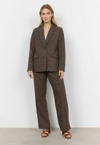 Brun ternet blazer og matchende brede bukser, lavet af tekstureret stof, med to frontlommer og en skrædderlavet pasform. Brune sandaler.