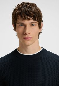 Navy textured sweater with a ribbed crew neckline. Close-fitting design with subtle woven pattern. Smooth fabric against the skin.