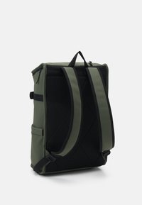 Sac à dos en tissu vert avec un dos en maille noire texturée, présentant deux bretelles rembourrées, une poignée supérieure et une poche latérale.