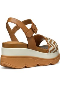 Sandal de cuero marrón con acentos tejidos en blanco, correa ajustable, gruesa plataforma blanca y suela de goma marrón texturizada.