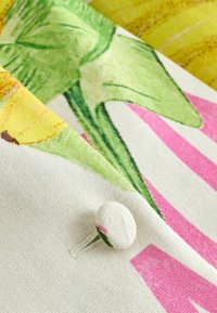 Gros plan d’un bouton recouvert de tissu sur un textile à motifs floraux et rayés avec des feuilles vertes, des couleurs jaunes et roses.