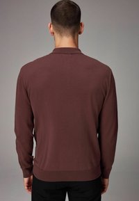 Maroon long-sleeve knit polo with a collar and ribbed cuffs, featuring a fitted waist and smooth texture, viewed from the back.