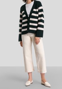 Raidallinen neulepusero tummanvihreänä ja kermanvärisenä, villasekoitetta, jossa on V-pääntie, nappikiinnitys ja rento istuvuus. Yhdistetty kermanvärisiin leveälahkeisiin housuihin.