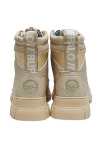 Zapatillas altas beige con un acabado texturizado, que presentan un logo circular, un forro estampado y una destacada marca blanca en el talón.