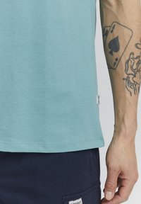 Gai zila kokvilnas T-kreklu ar apaļo kakla izgriezumu un īsām piedurknēm, ar mazu baltu etiķeti sānos un bez redzamām rakstām.