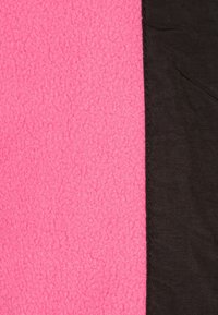 Tkanina polarowa w jasnym różowym kolorze po lewej stronie, przechodząca w gładki czarny materiał po prawej stronie, z widocznym szyciem i kontrastującymi fakturami.