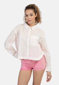 Camicia bianca corta con chiusura a bottone, caratterizzata da pois multicolori. Indossata con pantaloncini di jeans rosa chiaro. Maniche corte, include taschino sul petto.