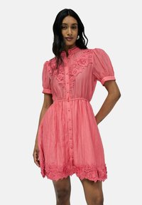 Vestido rosa de botones con mangas cortas abullonadas, que presenta una tela texturizada y un borde de encaje floral a lo largo del escote y el dobladillo.