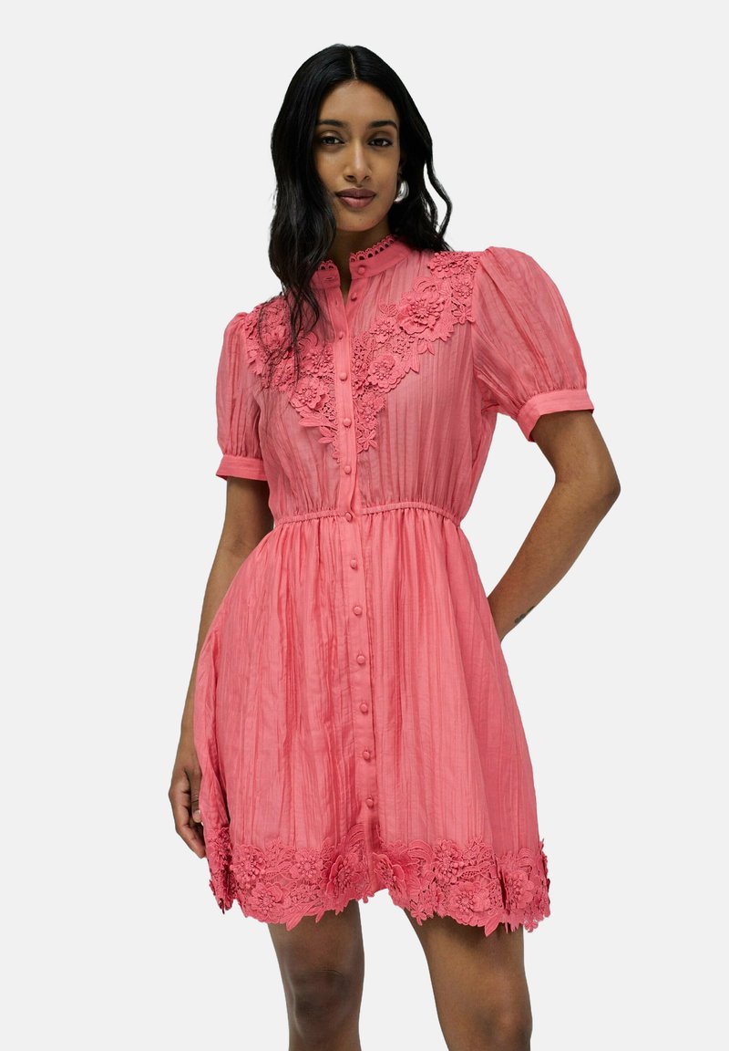 Vestido rosa de botones con mangas cortas abullonadas, que presenta una tela texturizada y un borde de encaje floral a lo largo del escote y el dobladillo.