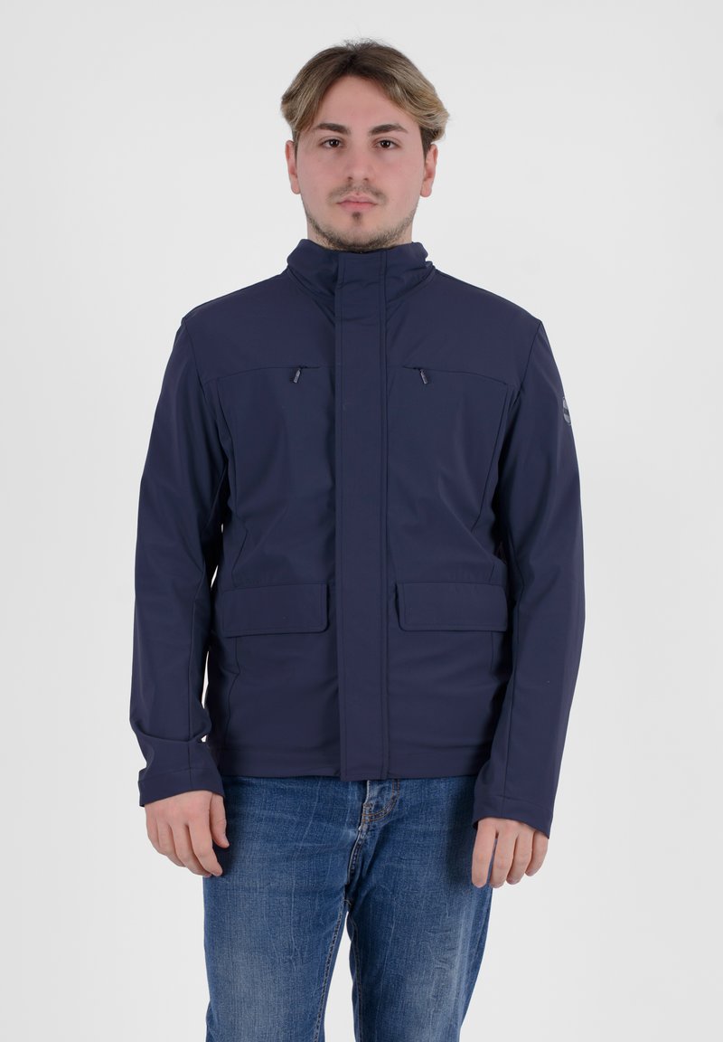 Giacca impermeabile blu navy con colletto alto, tasche con zip e una texture liscia. Caratteristiche includono maniche lunghe e tessuto resistente.