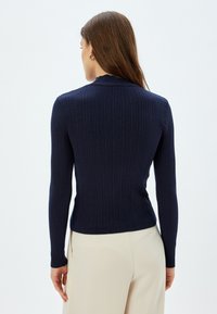 Marineblauer gerippter Strickpullover mit langen Ärmeln und rundem Ausschnitt, der eine figurbetonte Silhouette und eine glatte Textur aufweist.