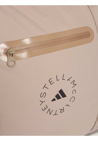 Beige rygsæk med en glat overflade, der har en blank tan lynlås og logo-print. Slankt design med en diskret frontlomme med lynlås.