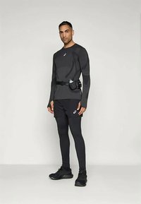 Black athletic long-sleeve top with texture details, paired with black shorts and leggings, featuring a belt with a hydration pouch and black sneakers.