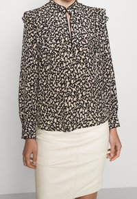 Svart och krämfärgad blus med tryck, rynkad krage och framknäppning, matchad med en krämfärgad blyertsskirt. Långa ärmar med knappribbor.