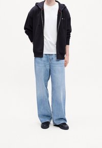 Černá mikina na zip s červenými doplňky, bílým tričkem s kulatým výstřihem, světle modré široké džíny a černé nazouvací boty. Minimalistický design.