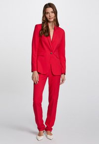 Completo rosso con giacca aderente dotata di rever a risvolto e un solo bottone. Pantaloni su misura con gamba dritta. Tessuto dalla finitura liscia.