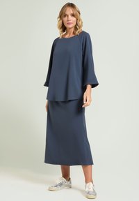 Mörkblå långärmad topp lagd över en matchande midikjol, med avslappnad passform och slät textur. Matchad med silverfärgade sneakers.