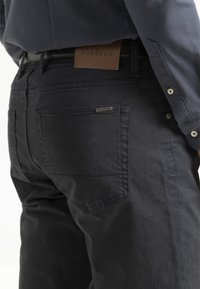 Los jeans de mezclilla negra cuentan con una textura suave, un diseño minimalista, bolsillos traseros prominentes y una etiqueta de cuero en la cinturilla.
