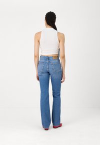 Hoge taille blauwe denim flared jeans met een lichtbruine label aan de achterkant, gecombineerd met een strak wit mouwloos topje. Gladde textuur, casual ontwerp.