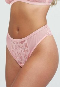 Lichtroze lingerie met florale kantdetails, getoond rond de taille van een persoon, waarmee het ontwerp en de textuur van de stof worden benadrukt.